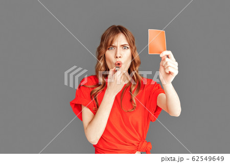 Freestyle. Woman in sports clothes studio standing isolated on grey with red card whistling angry close-up