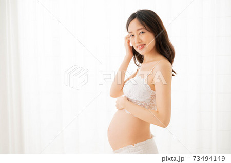 A Pregnant Woman Topless in Pajama Pants in Profile in a Home